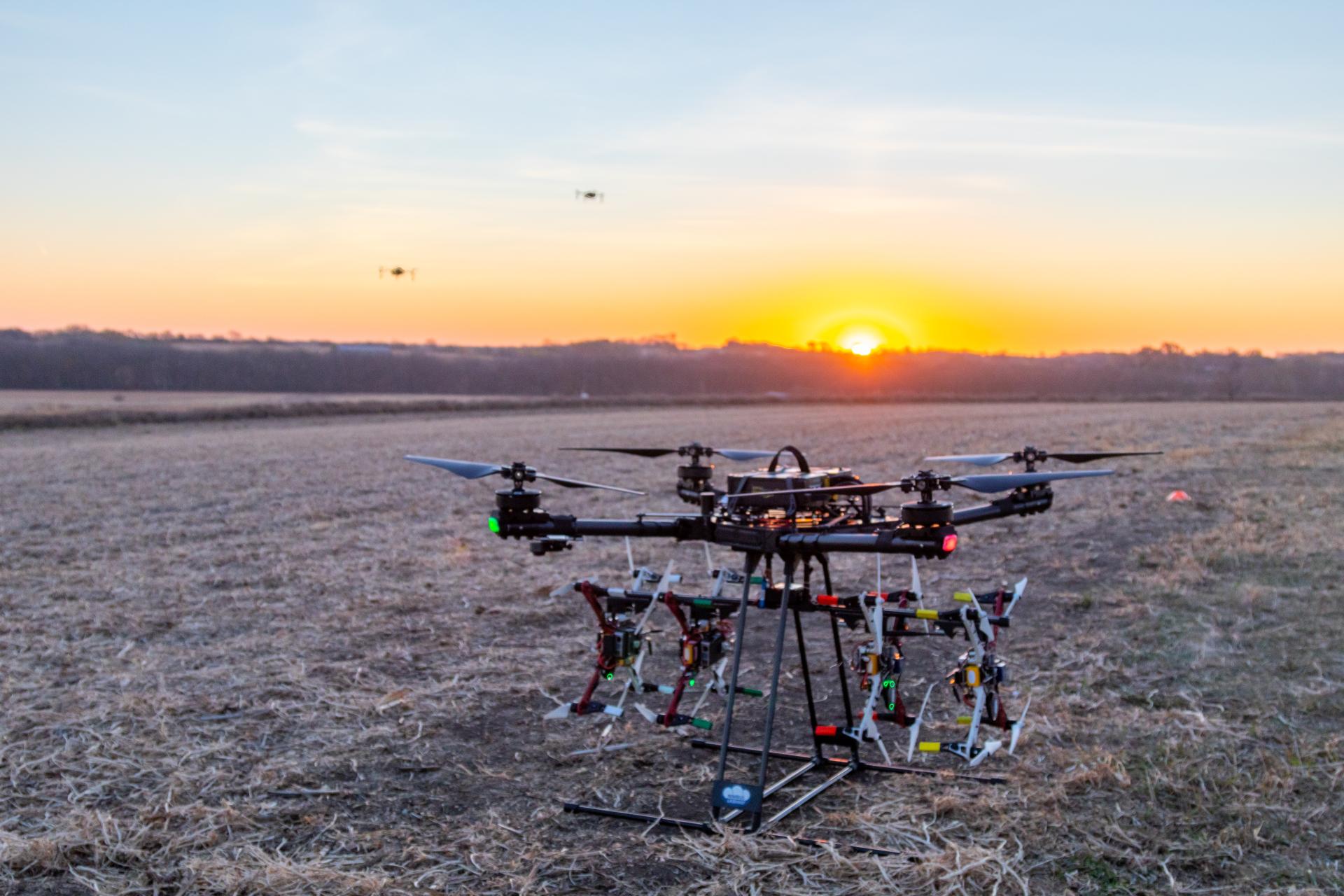 Large drone carrying 4 small drones at sunrise with two small drones hovering in background